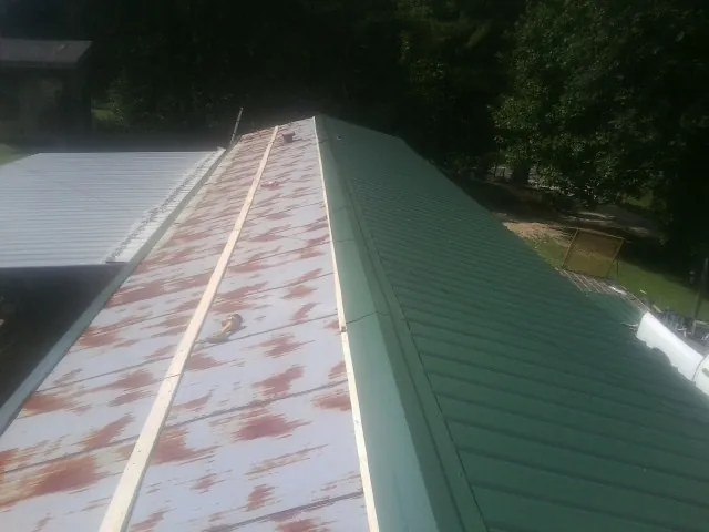 Old rusted panels beside newly installed green metal roofing — Wind Damage Roof Repair by Roofing Brothers in Millington