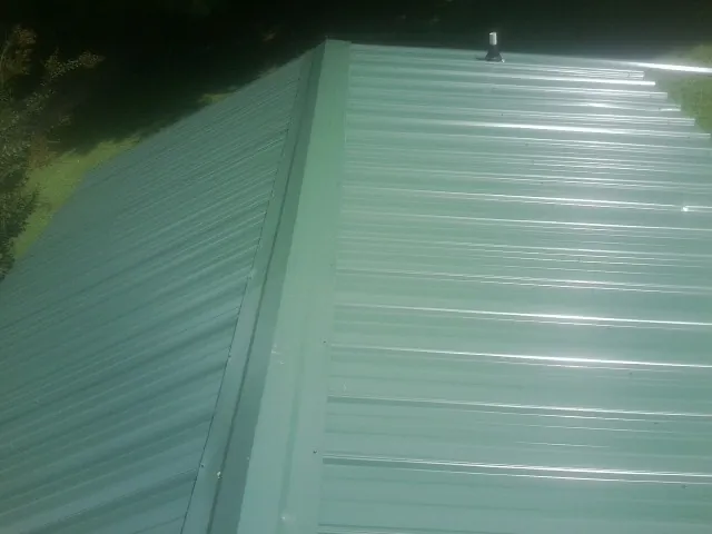 New green metal panels meeting at the ridge of a roof — Flat Roof Repair work by our crew in Millington